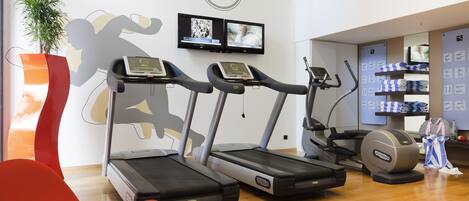A gym with treadmills, a red chair, a wall clock, and exercise equipment.