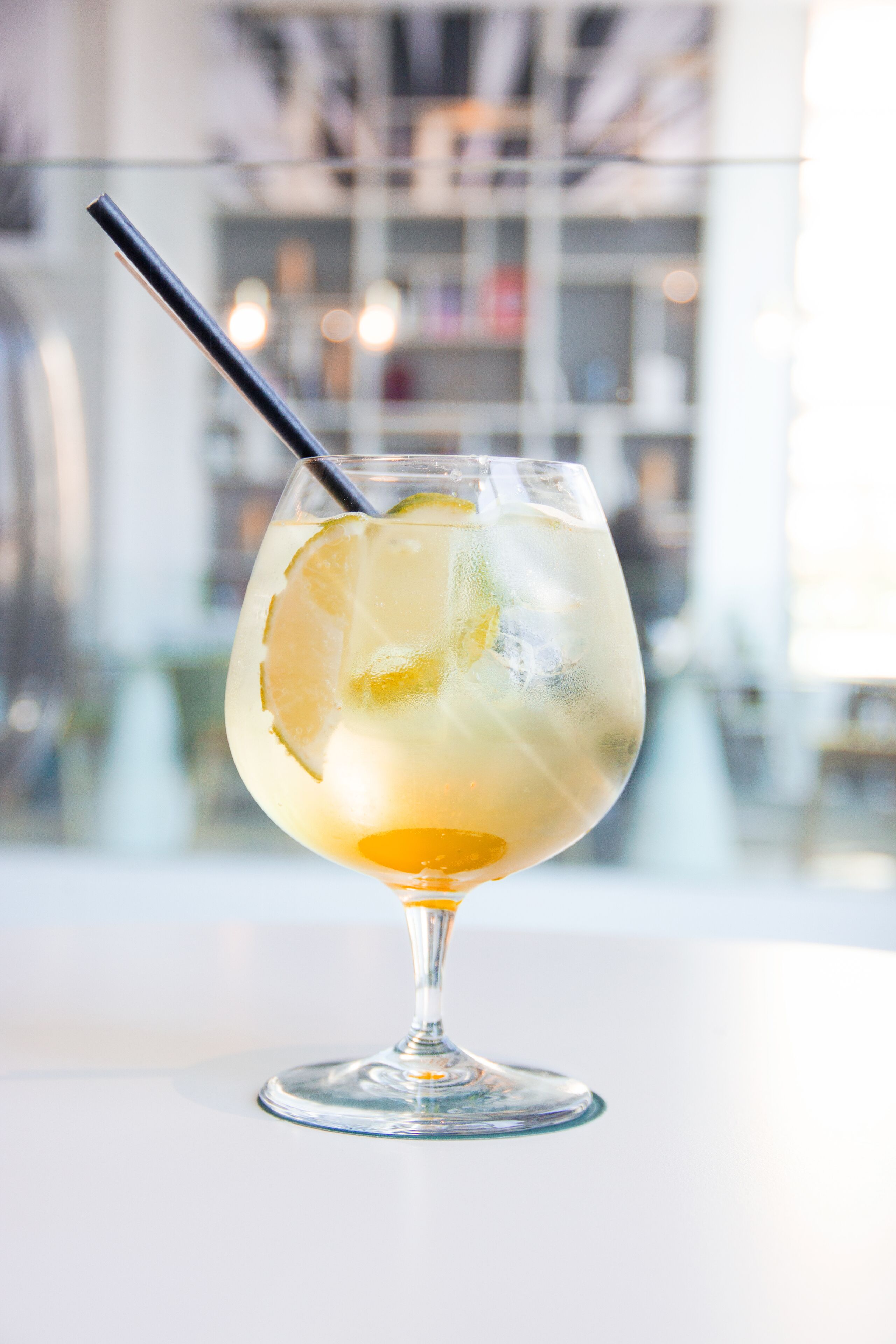 A cocktail glass with a lemon slice and a straw on a white surface.