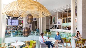 A modern hotel lobby with a central bar, seating areas, and a large screen displaying the hotel name.