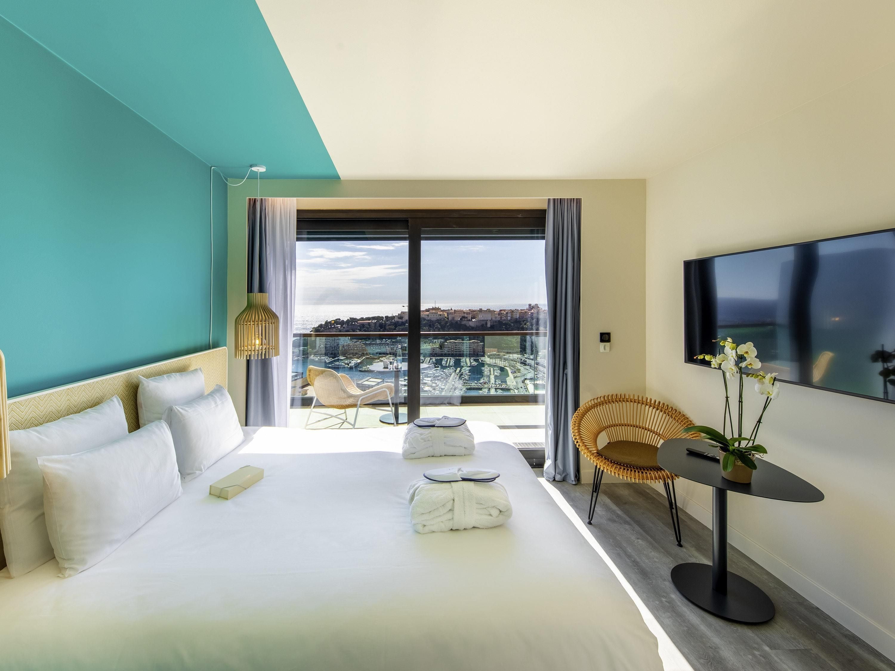 Habitación de hotel con cama, televisión, balcón y vistas a la ciudad, además de una silla.
