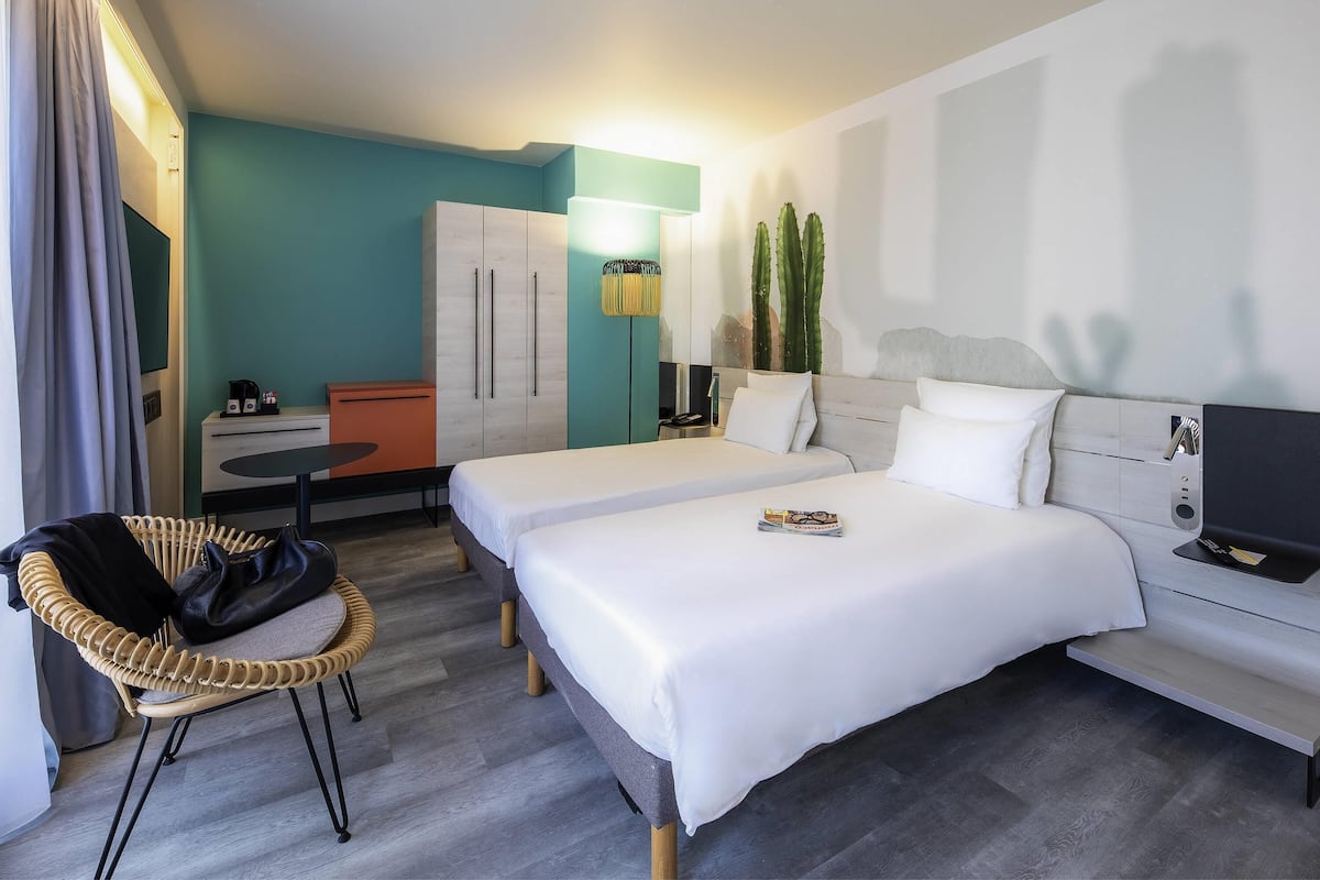 Ein Hotelzimmer mit zwei Betten, einem Schreibtisch, einem Stuhl, einem Kleiderschrank und einem Fernseher.