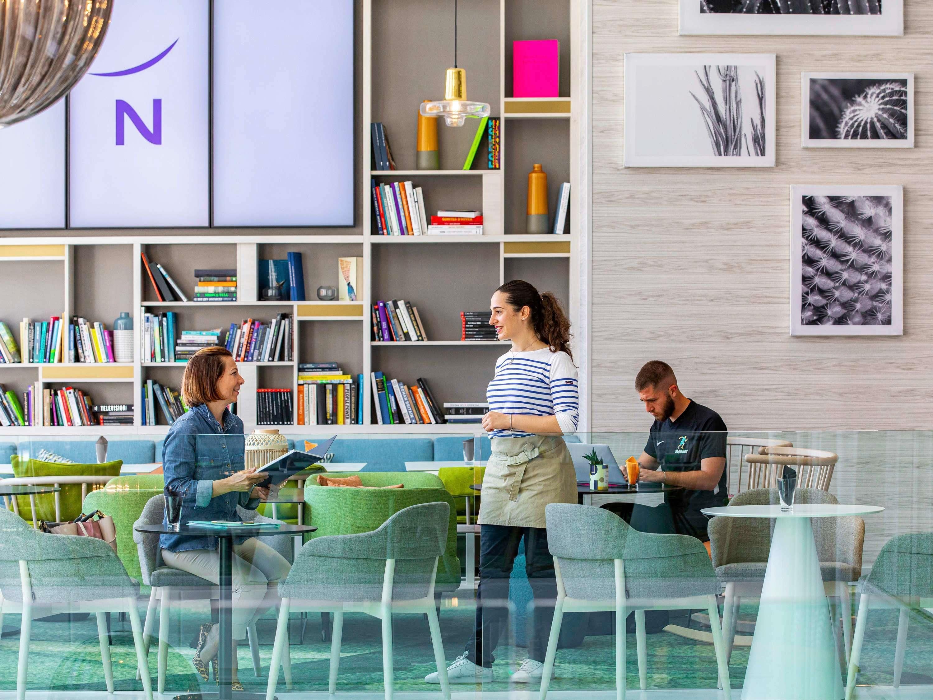 A modern library with bookshelves, a coffee bar, and a seating area with tables and chairs.