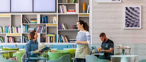 A modern library with bookshelves, a coffee bar, and a seating area with tables and chairs.