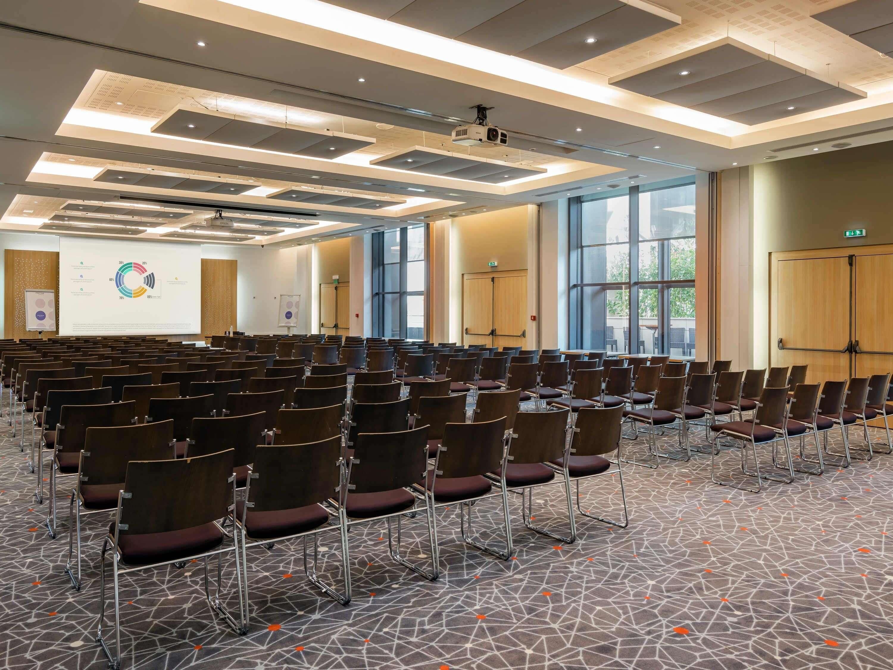 Een vergaderzaal met rijen stoelen, een projecteerder en een presentatiescherm.