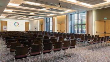 Een vergaderzaal met rijen stoelen, een projecteerder en een presentatiescherm.