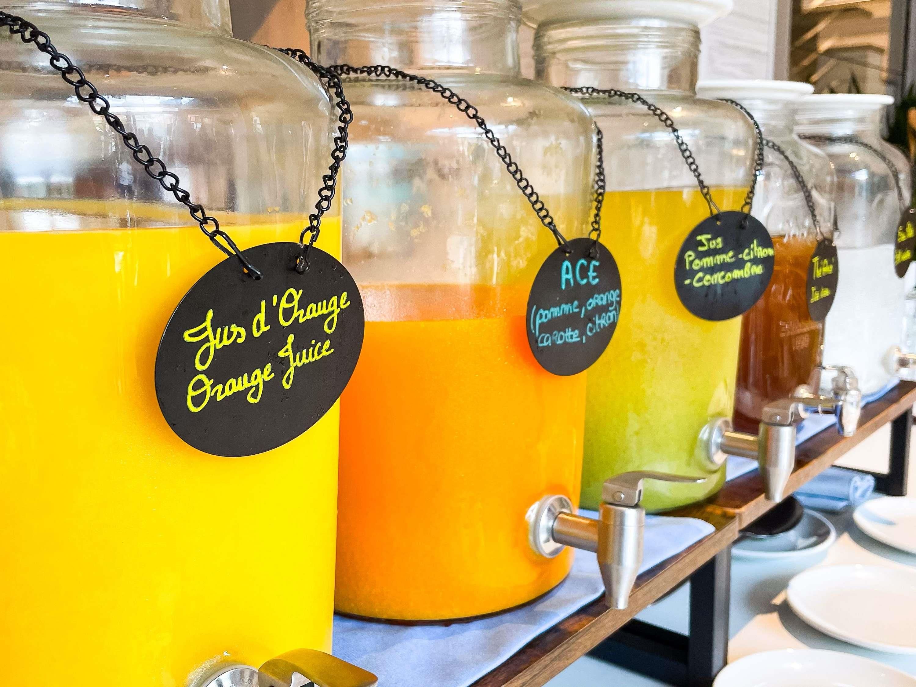Una barra de jugos con dispensadores etiquetados para jugo de naranja, jugo de manzana y jugo de pera.