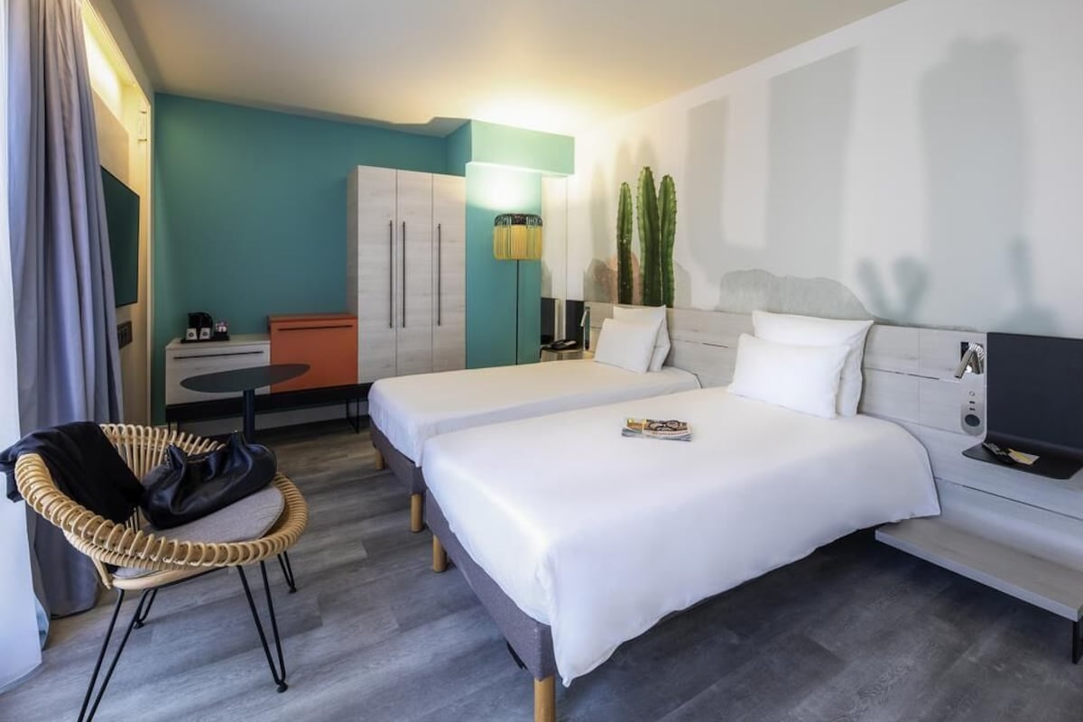 Een hotelkamer met twee bedden, een bureau, een stoel, een televisie en een plant.