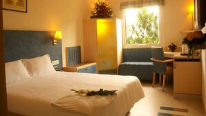 Habitación de hotel con cama, escritorio, silla, armario, ventana y una lámpara.