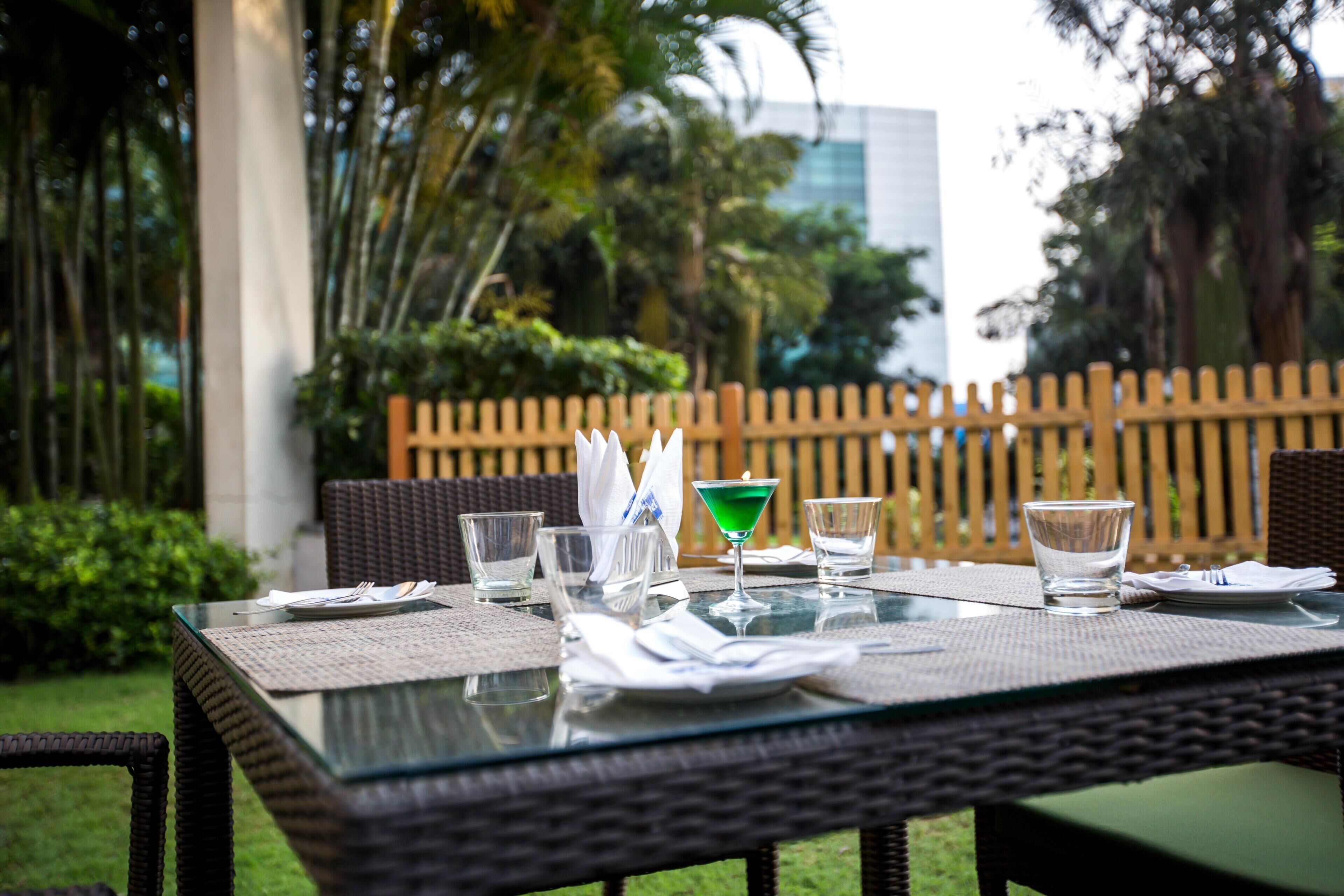 An outdoor dining table with clear glassware, a green cocktail, and a menu.