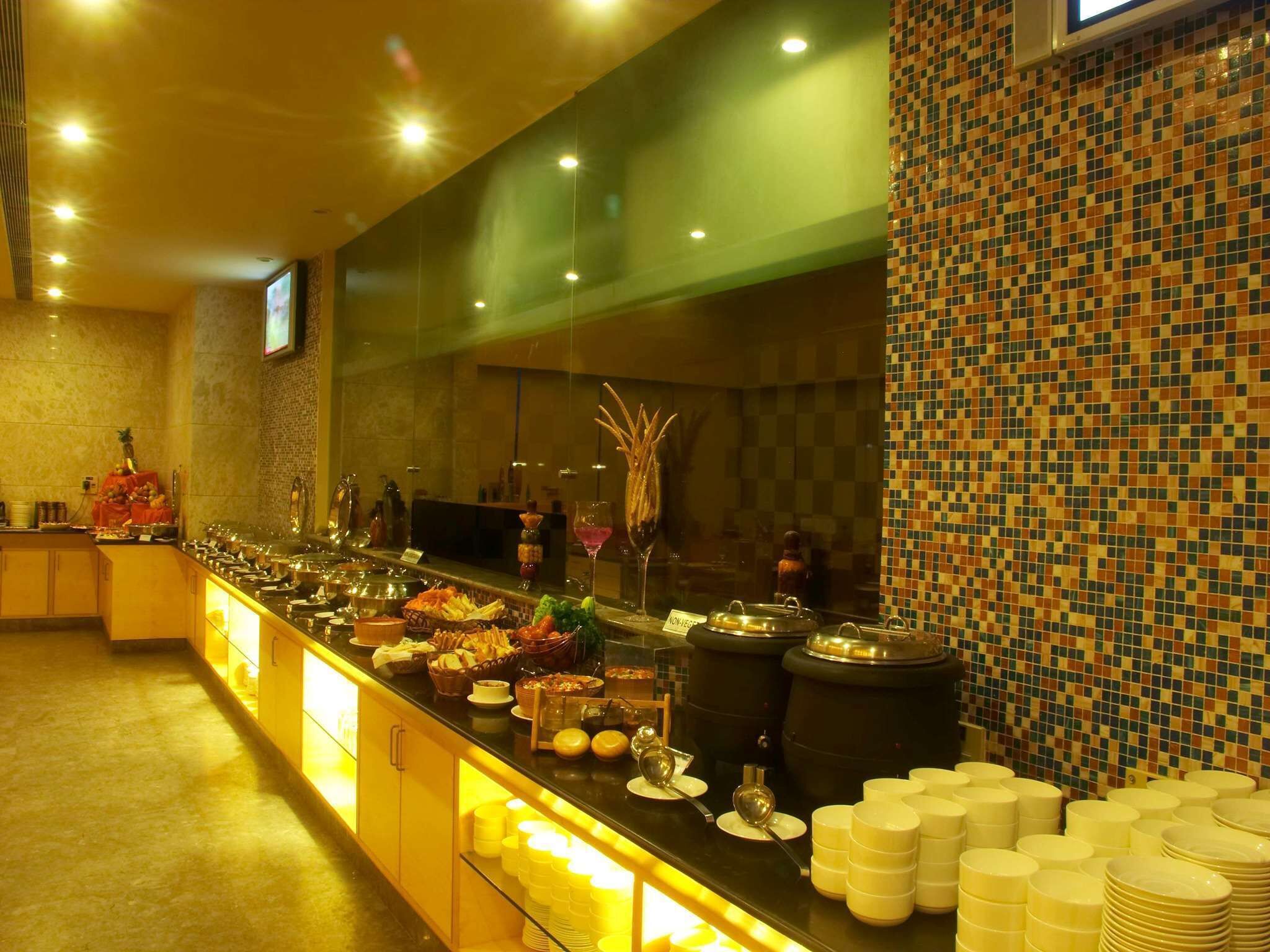 A buffet setup with various food items and utensils, a tiled wall, and a television screen.