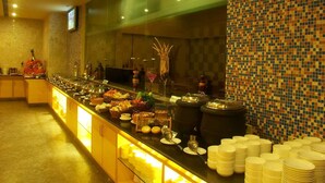 A buffet setup with various food items and utensils, a tiled wall, and a television screen. - Radha Hometel Whitefield (Bengaluru)