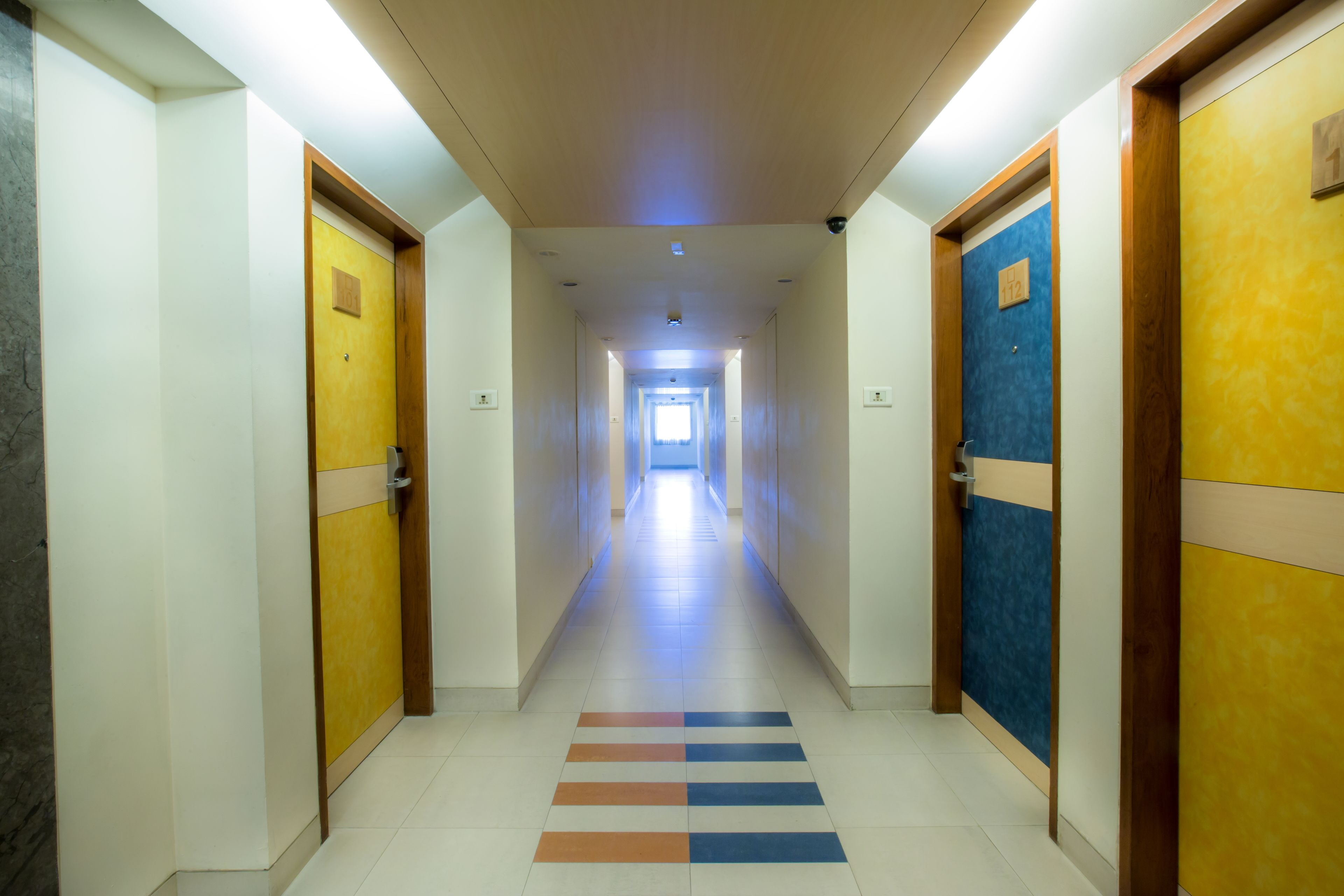 A hotel corridor with doors on both sides, a tiled floor, and a ceiling light.