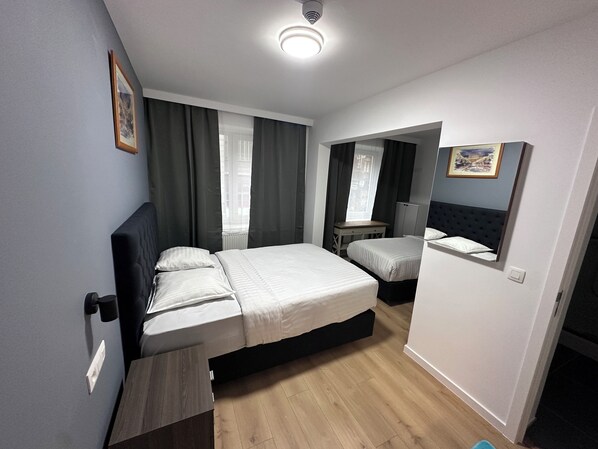 A modern bedroom with a large bed, a bedside table, a mirror, and a window with curtains.