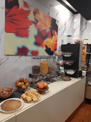 A buffet setup with various food items, a coffee machine, and a decorative leaf painting on the wall.