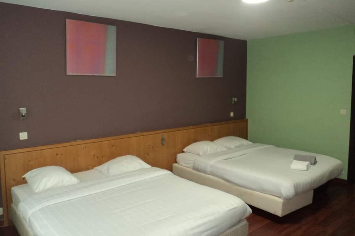 A room with two single beds, a wooden headboard, a green wall, and a ceiling light.