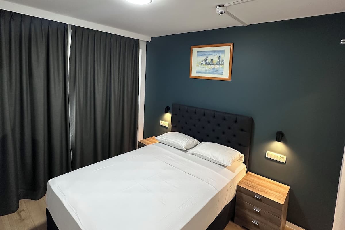 A modern hotel room with a large bed, dark walls, and a cityscape painting.