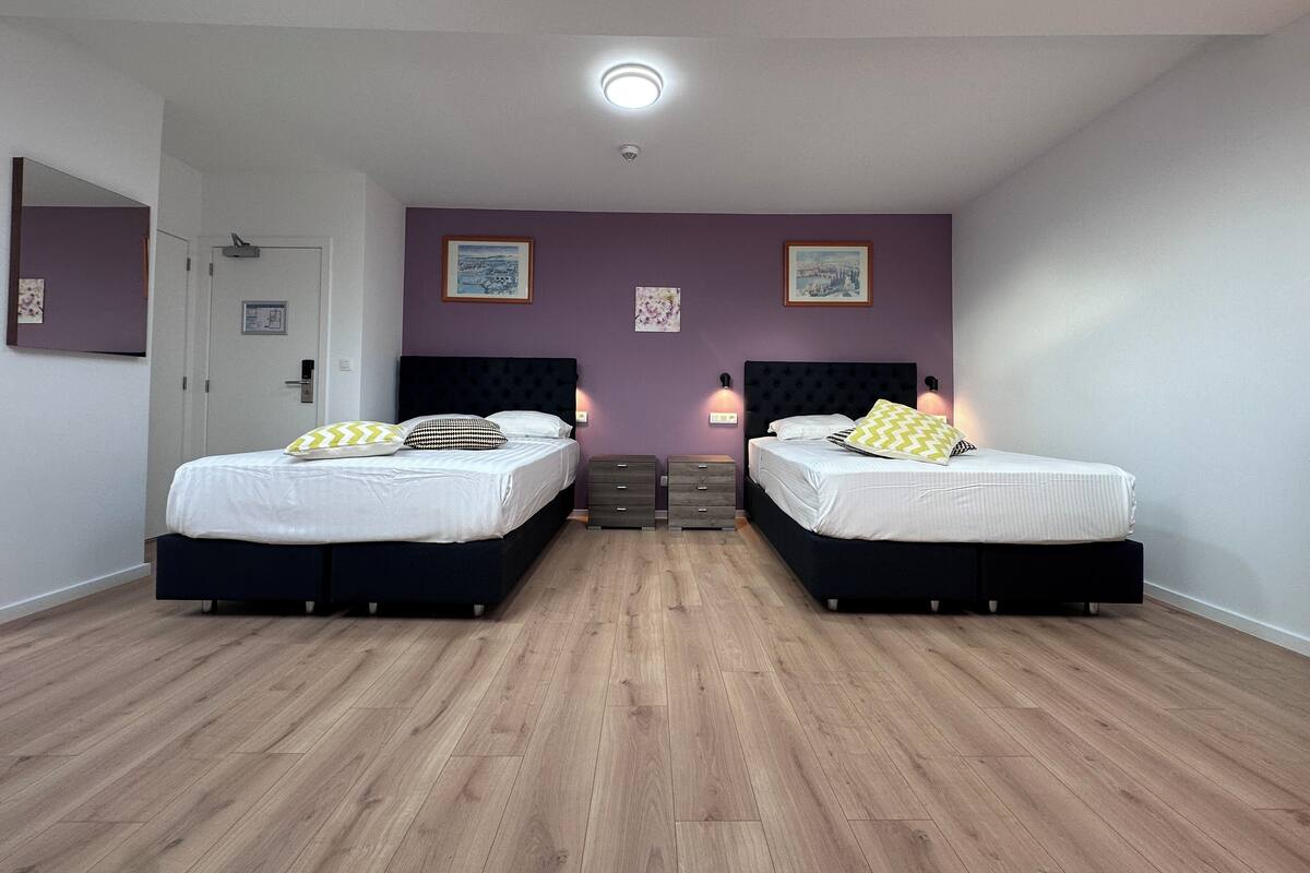 A modern bedroom with two beds, wooden flooring, and purple walls.