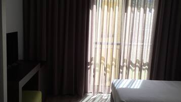 A hotel room with a bed, a desk, and a view of the outside through sheer curtains.