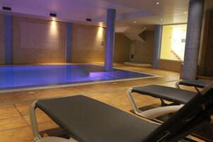 Un área de piscina con sillas de descanso, paredes enlosadas y una escalera que conduce a un nivel superior.