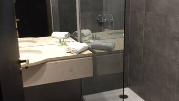 Ein modernes Badezimmer mit einer gläsernen Duschkabine, einem Waschbecken mit Pflegeprodukten und einem Holzboden.