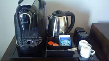 Una cafetera, un hervidor, una jarra de café, una caja de té y dos tazas blancas sobre una bandeja.