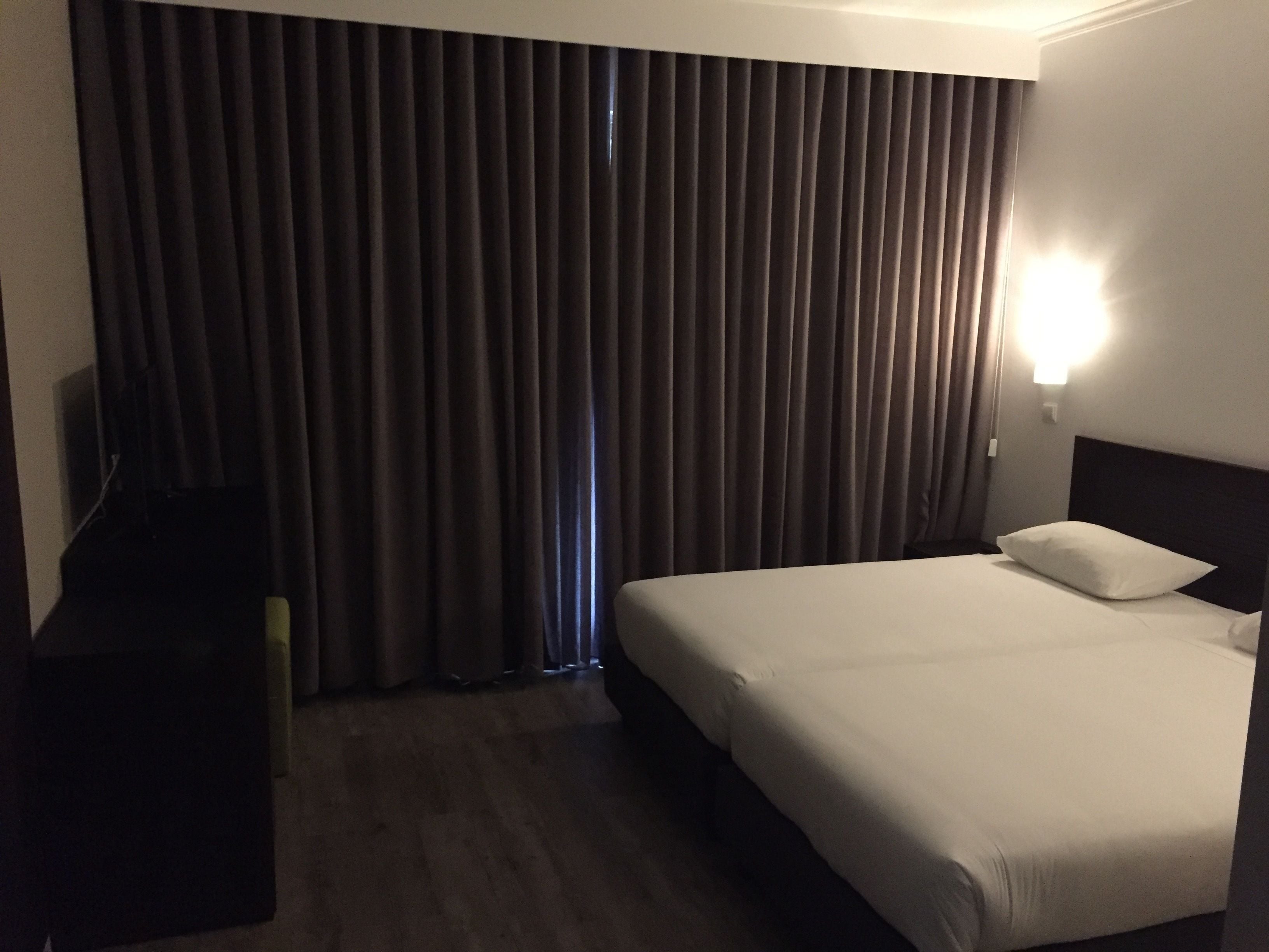 Una habitació d'hotel amb un llit, una taula de nit, una televisió i una cortina.