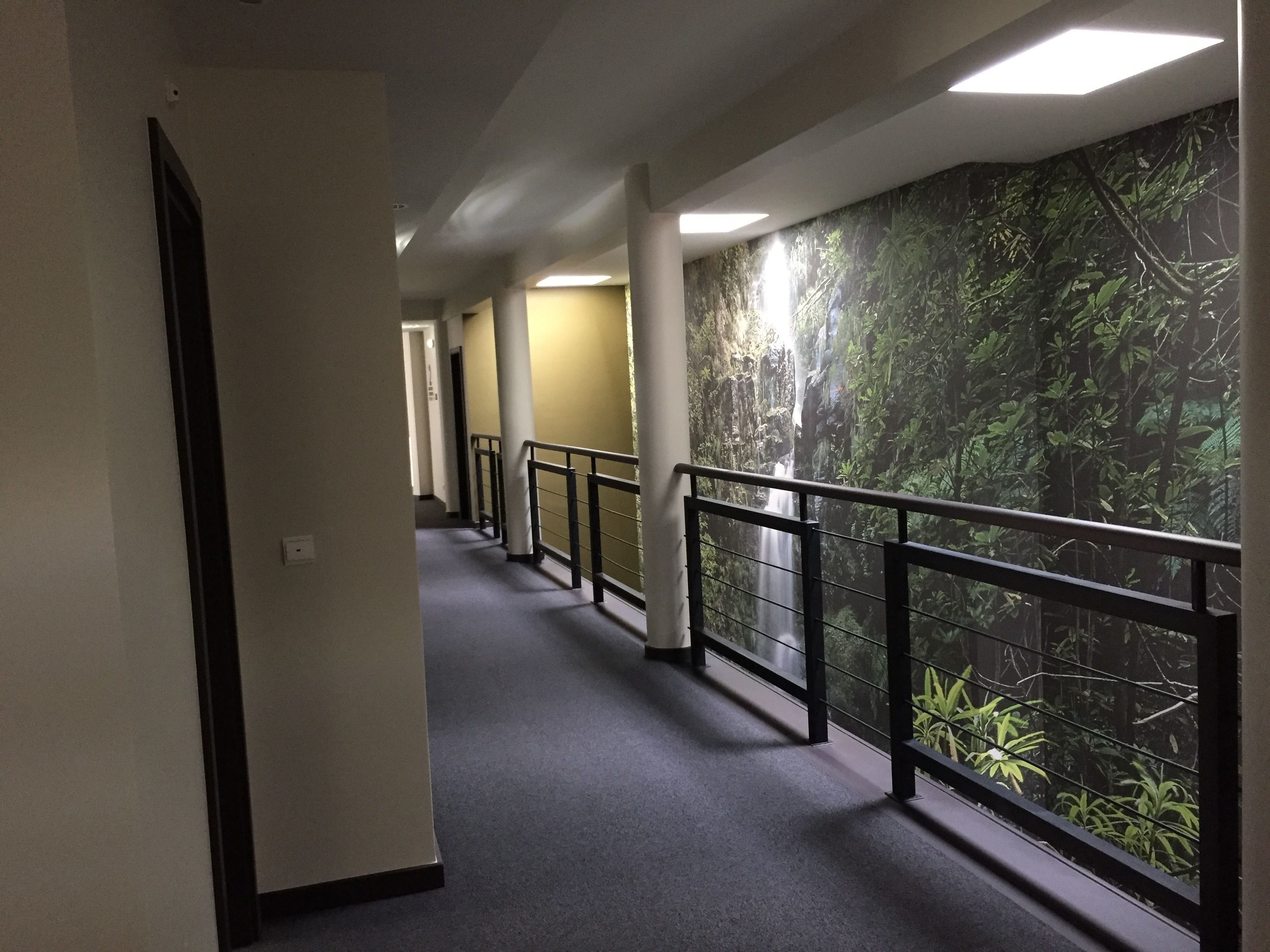 A hallway with a mural of a forest, a grey carpet, and a black railing.