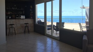 A spacious room with a bar area, a large sliding glass door leading to a balcony with a view of the ocean. - Hotel Euro Moniz (Porto Moniz)