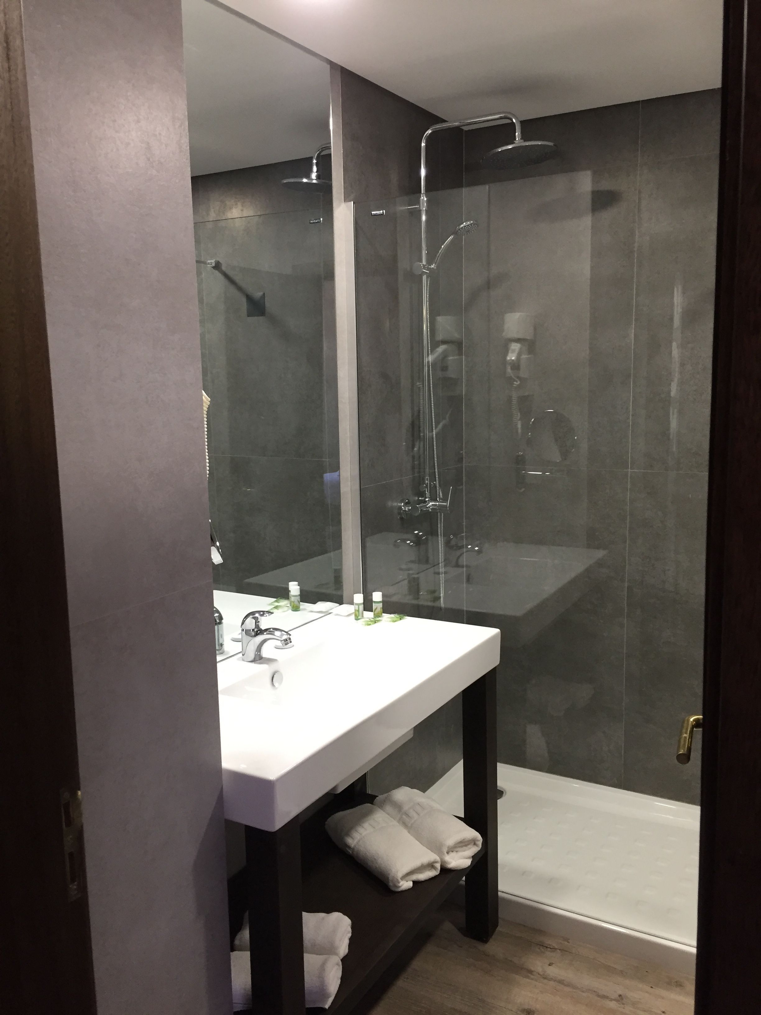 Een moderne badkamer met een douchecabine van glas, een witte wastafel met toiletartikelen en een donkere houten wastafelmeubel.
