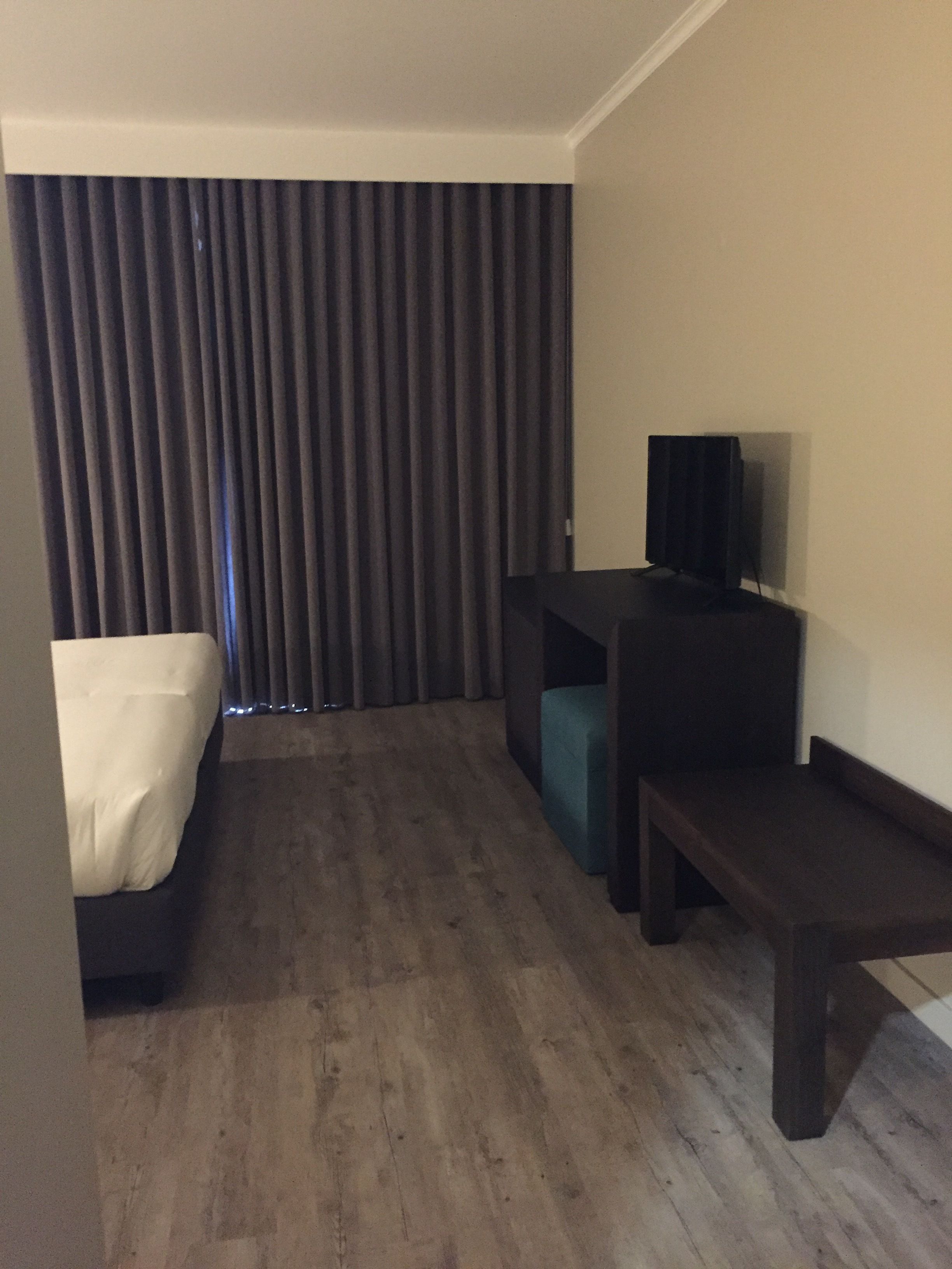A hotel room with a bed, a desk, a television, and a bench.