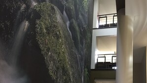 A spacious lobby with a large mural of a waterfall, a staircase leading to an upper level, and a modern pillar. - Hotel Euro Moniz (Porto Moniz)