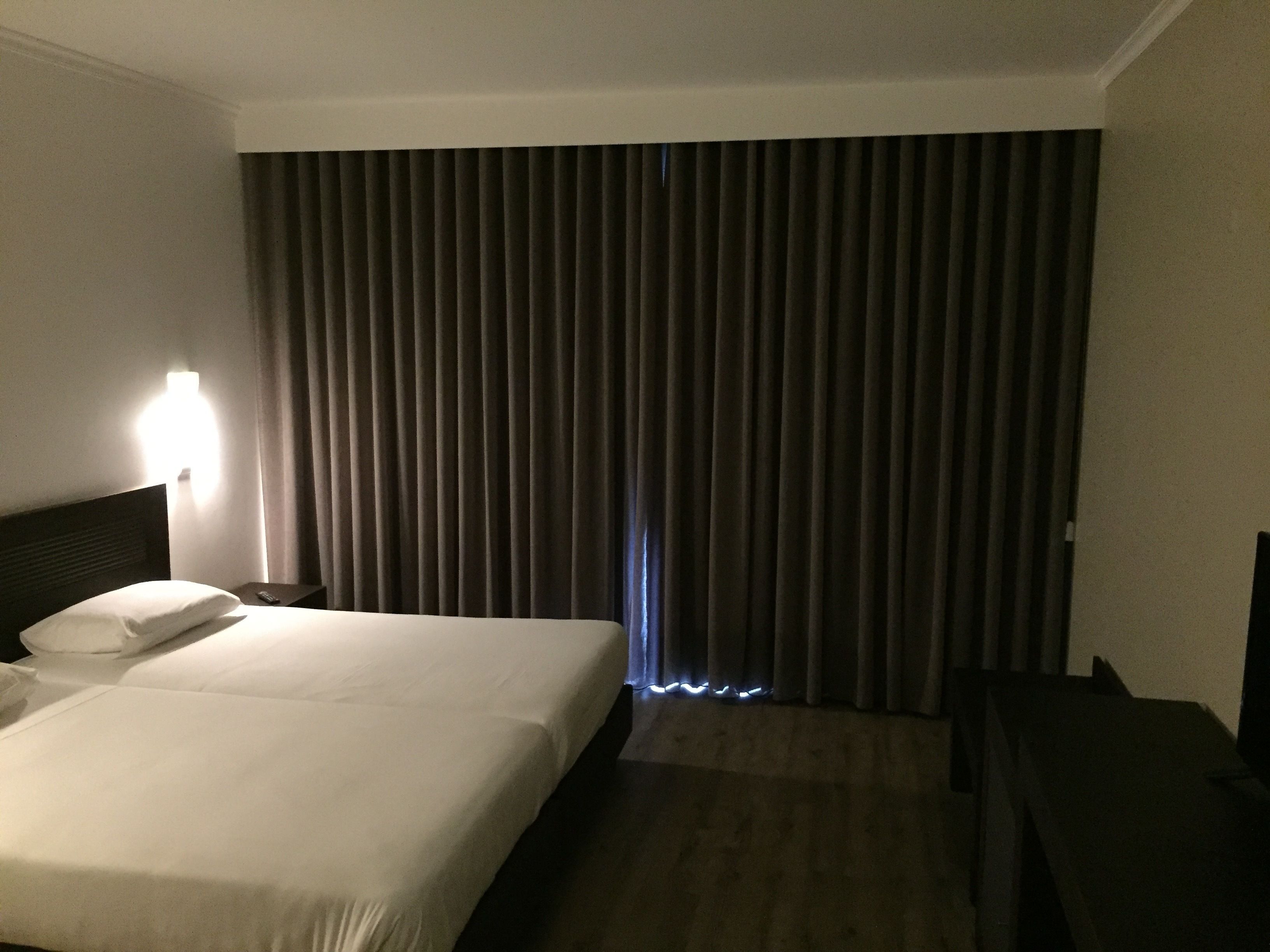 A hotel room with a bed, a nightstand, a lamp, and a window with curtains.