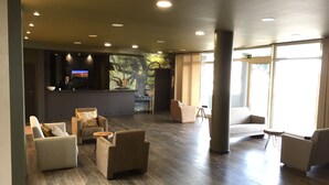 A spacious lobby with multiple seating areas, a reception desk, and a large window providing natural light. - Hotel Euro Moniz (Porto Moniz)