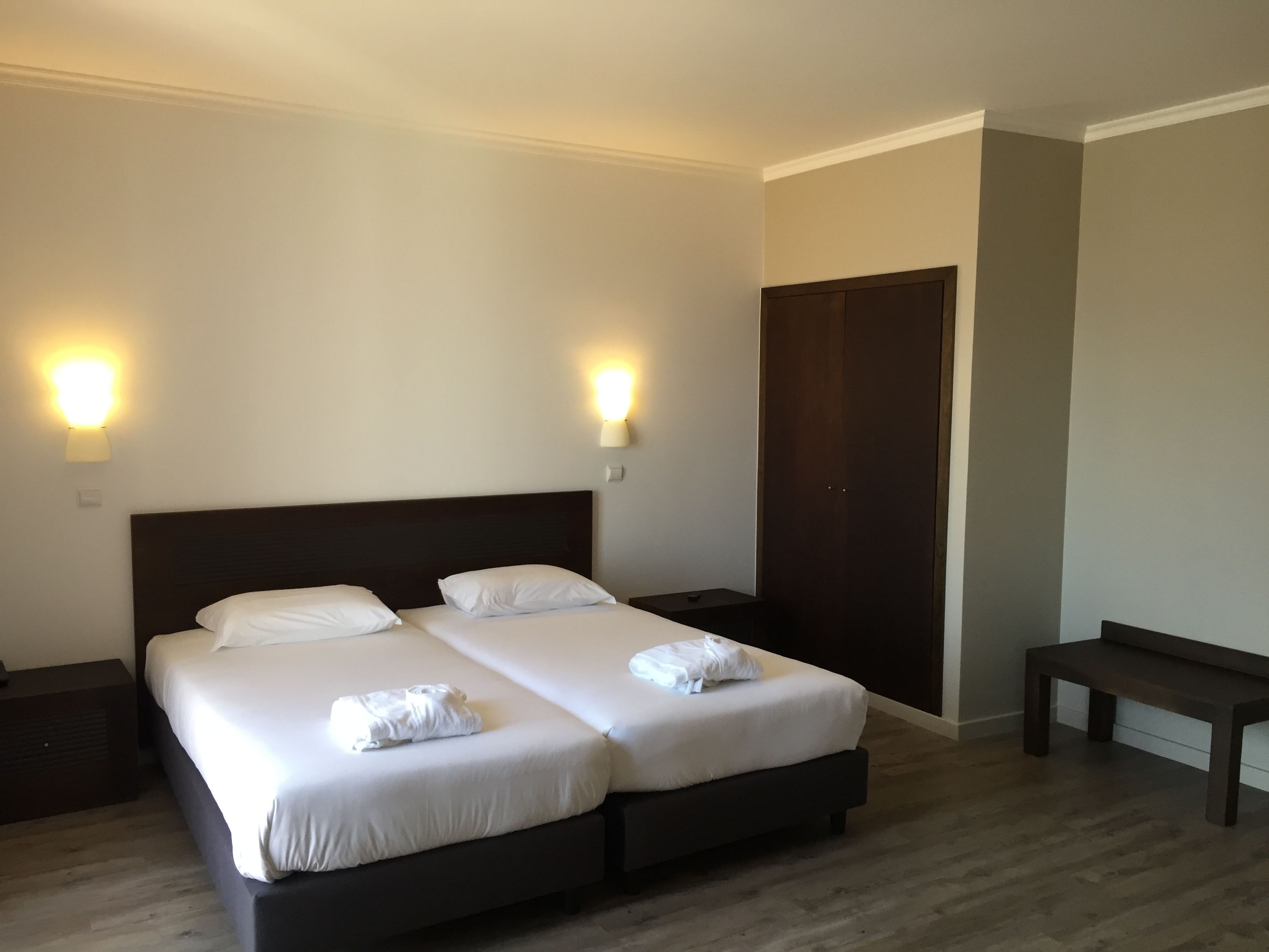 Ett hotellrum med två sängar, sänglampor, en träbänk och en garderob.