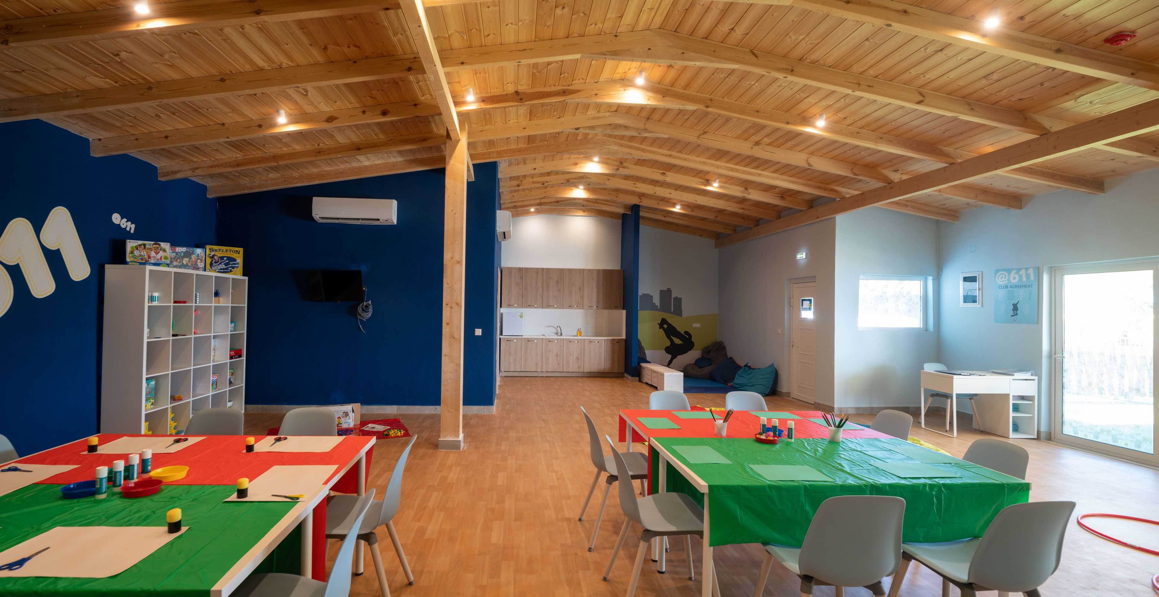 Una habitación amplia con vigas de madera en el techo, una pared azul con el número '11', una estantería blanca y una mesa verde con sillas.