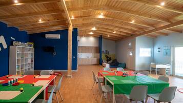 Una habitación amplia con vigas de madera en el techo, una pared azul con el número '11', una estantería blanca y una mesa verde con sillas.
