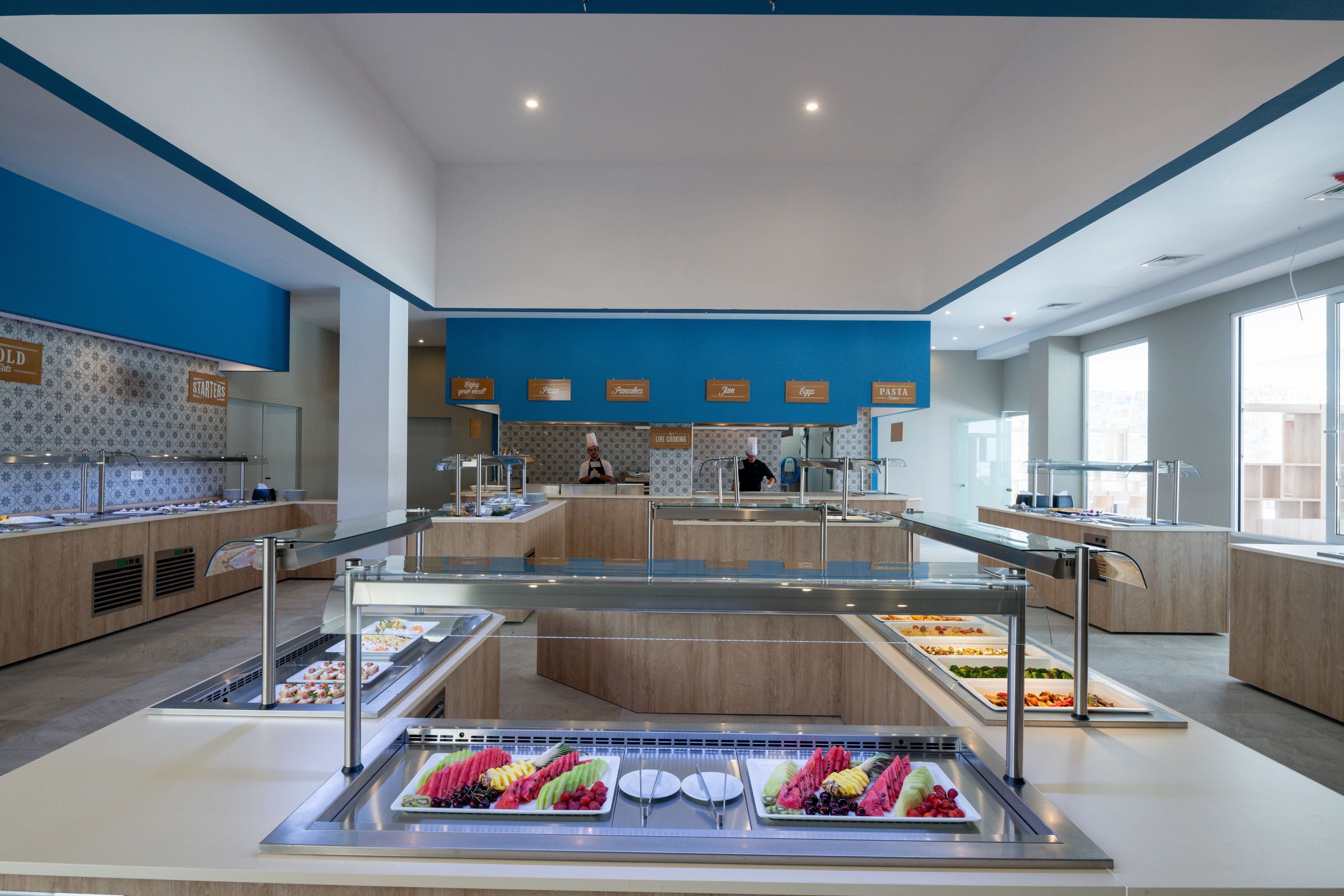 A modern buffet area with multiple food stations, including a fruit display and a variety of prepared dishes.