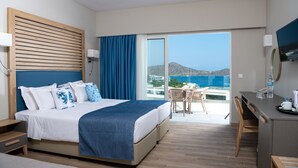 Une chambre d’hôtel moderne dotée d’un grand lit, d’un bureau et d’un balcon offrant une vue sur la mer.