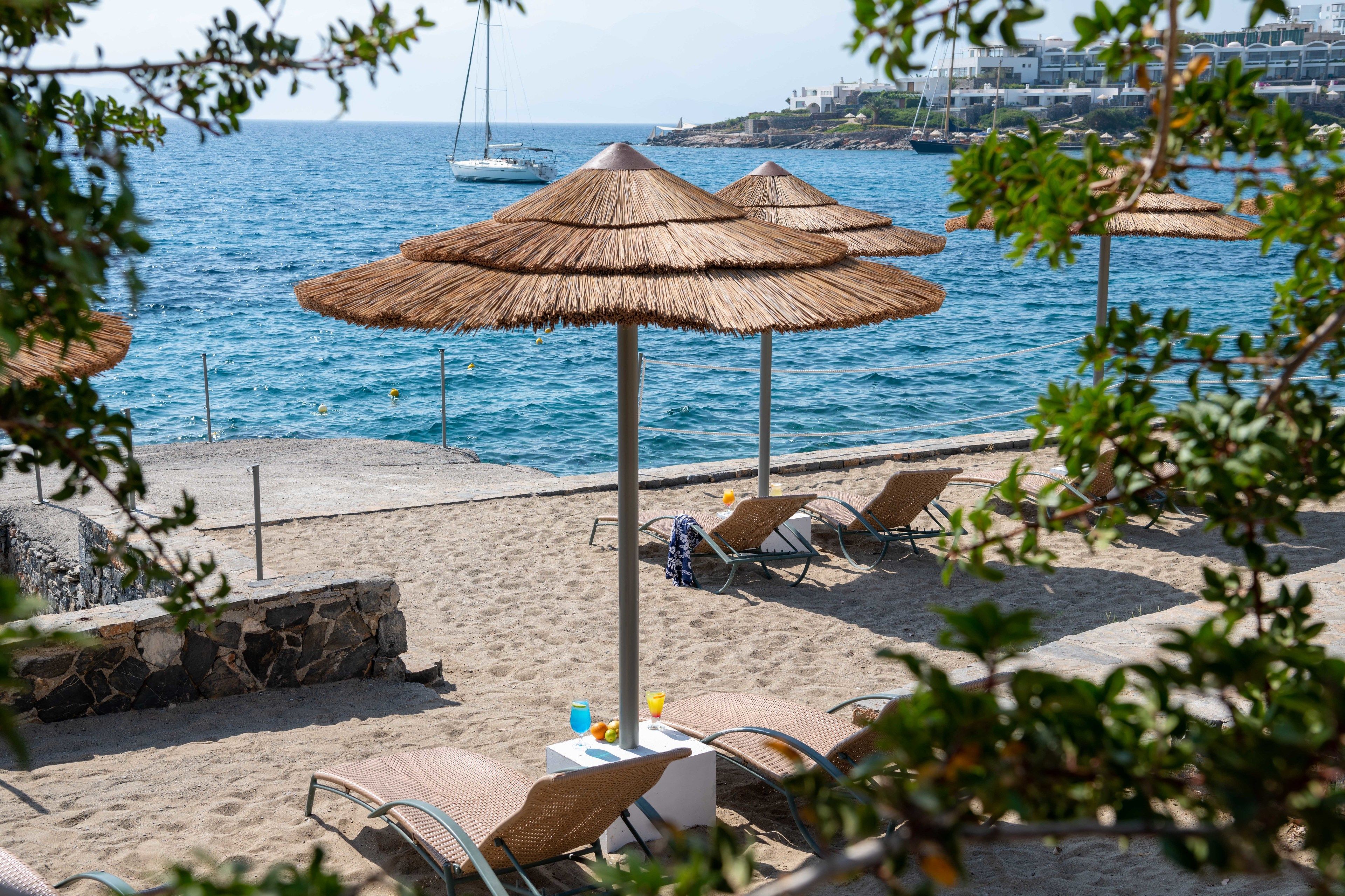 A beachside setting with thatched umbrellas, lounge chairs, and a table with a drink and fruit.