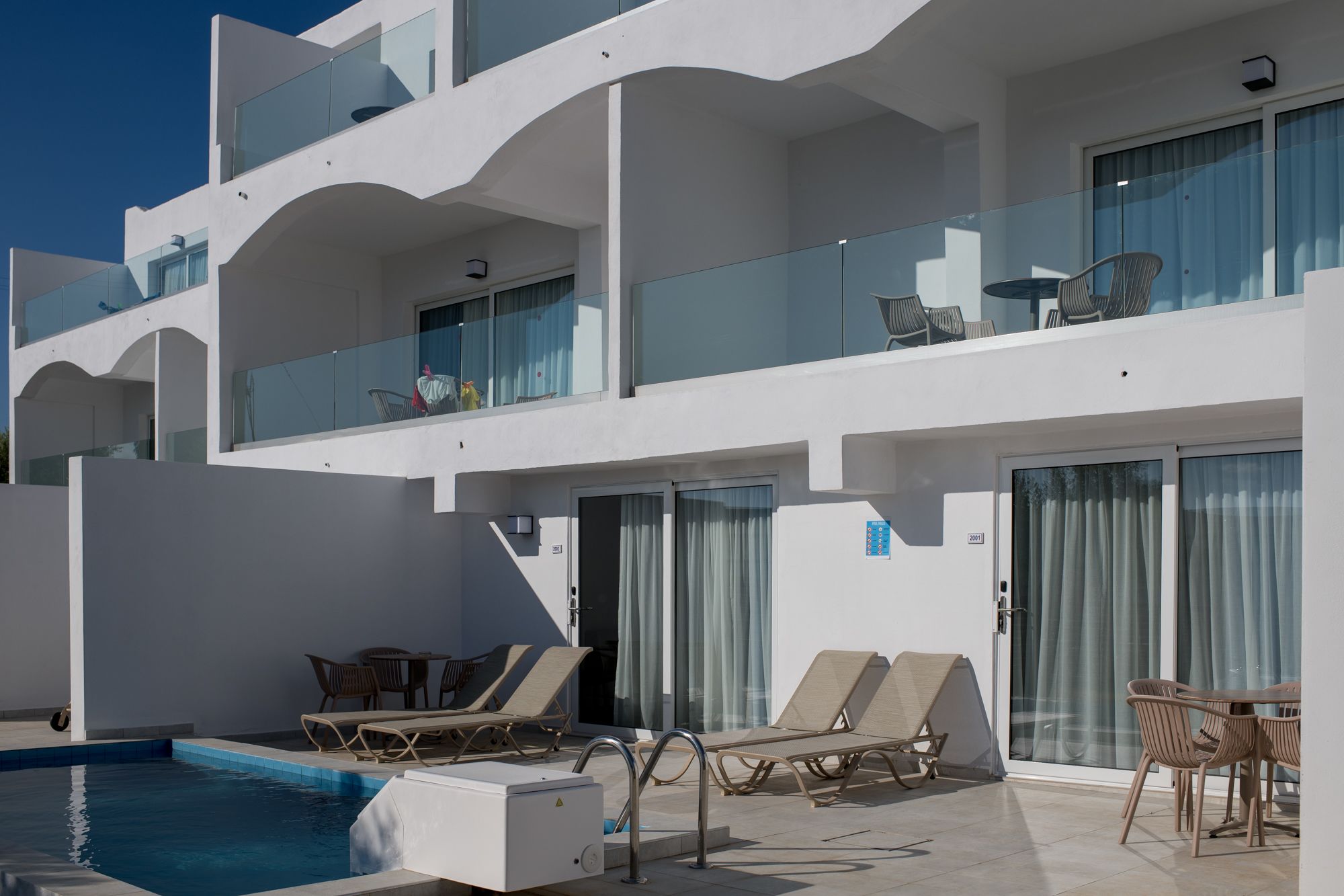 Et moderne hotel med poolområde, liggestole og gelænder af glas.