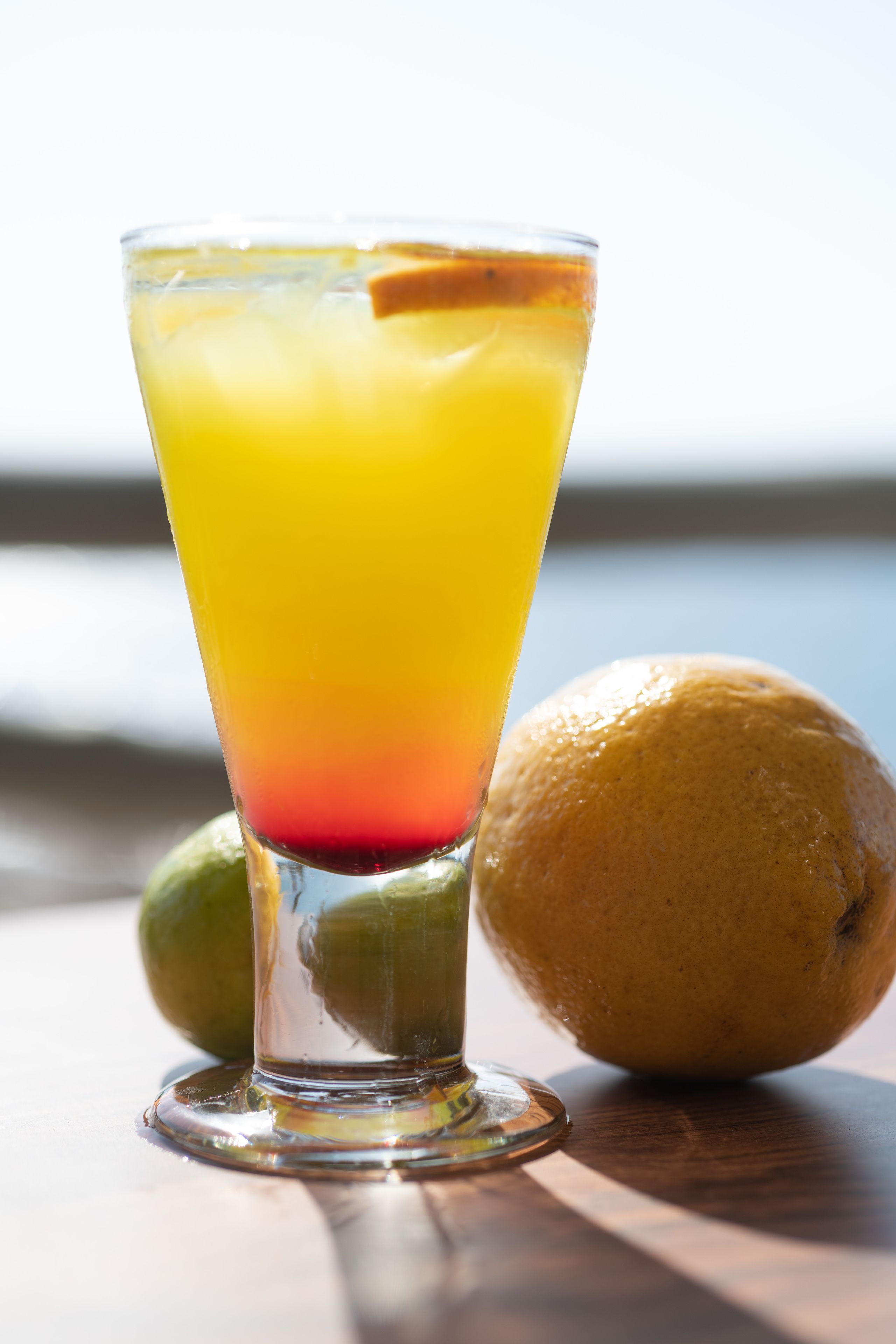 A tall glass with a gradient drink, a lemon, and a lime on a wooden surface.