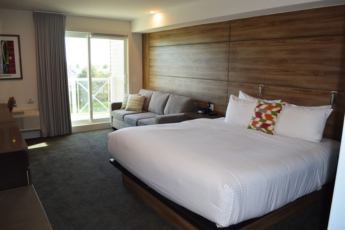 A hotel room with a large bed, a sofa, a desk, and a balcony with curtains.