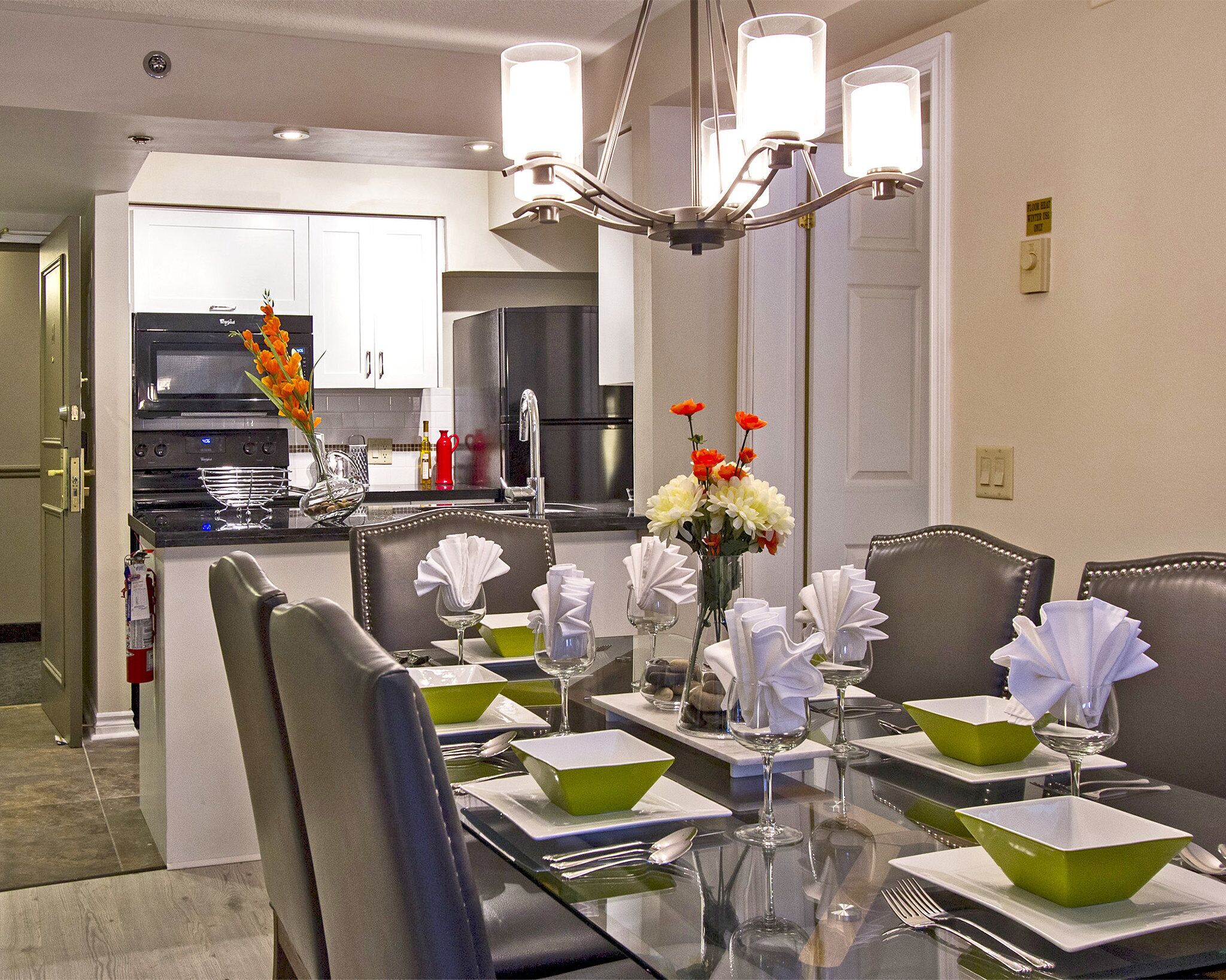 A dining area with a glass table set for a meal, chairs, and a vase with flowers.