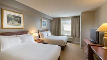 A hotel room with two beds, a desk with a lamp, a TV, and two framed pictures on the wall.