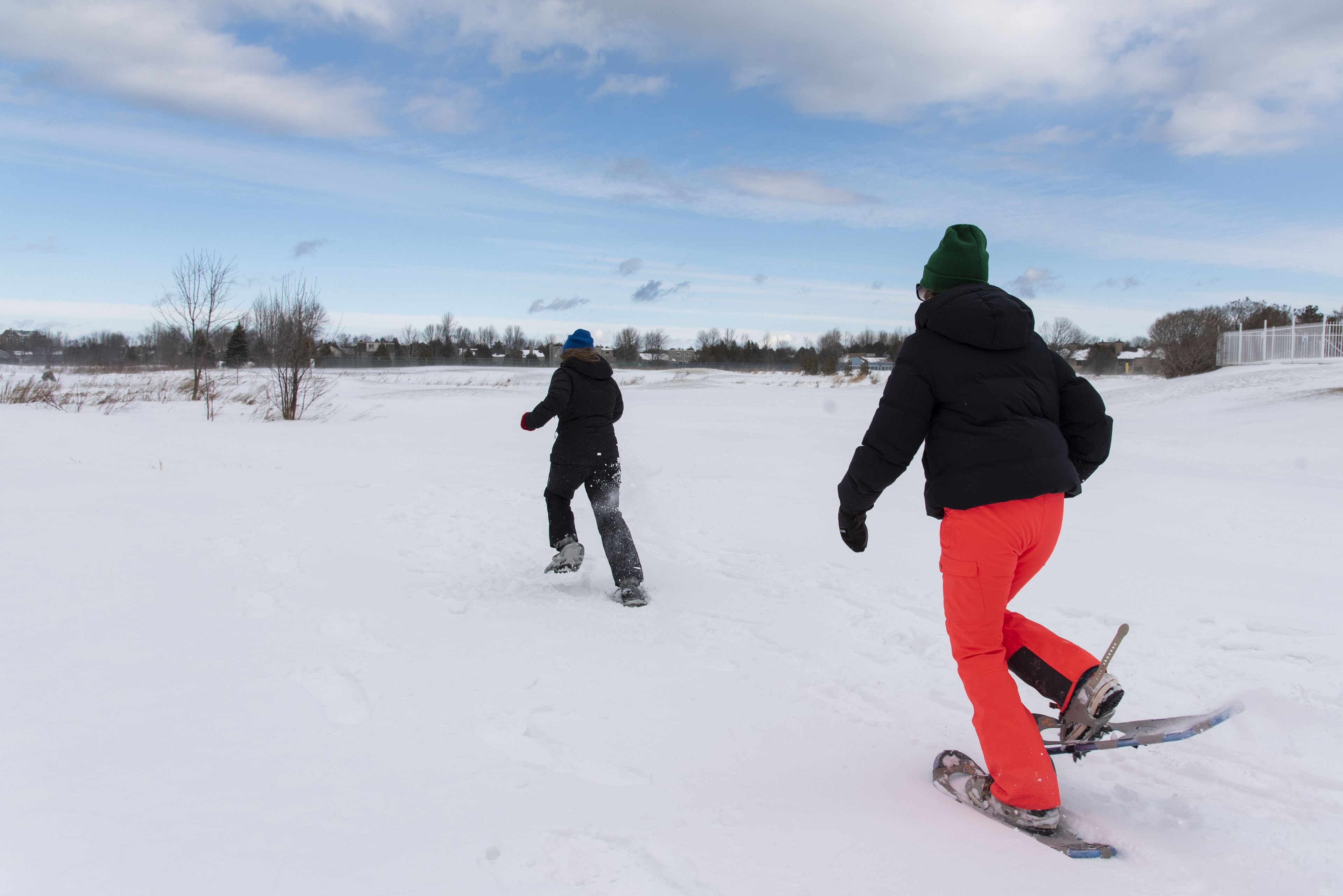 Dos personas hacen snowboard sobre una superficie nevada y plana, con cielo despejado al fondo.