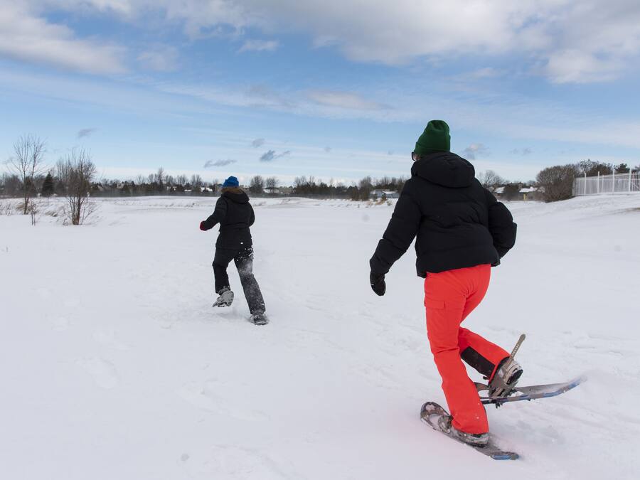 Dos personas hacen snowboard sobre una superficie nevada y plana, con cielo despejado al fondo.