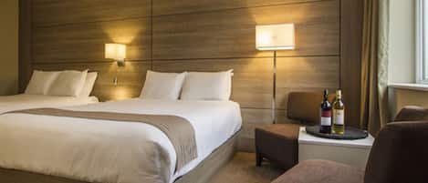 A hotel room with a large bed, two bedside lamps, a small table with a bottle, and a chair.