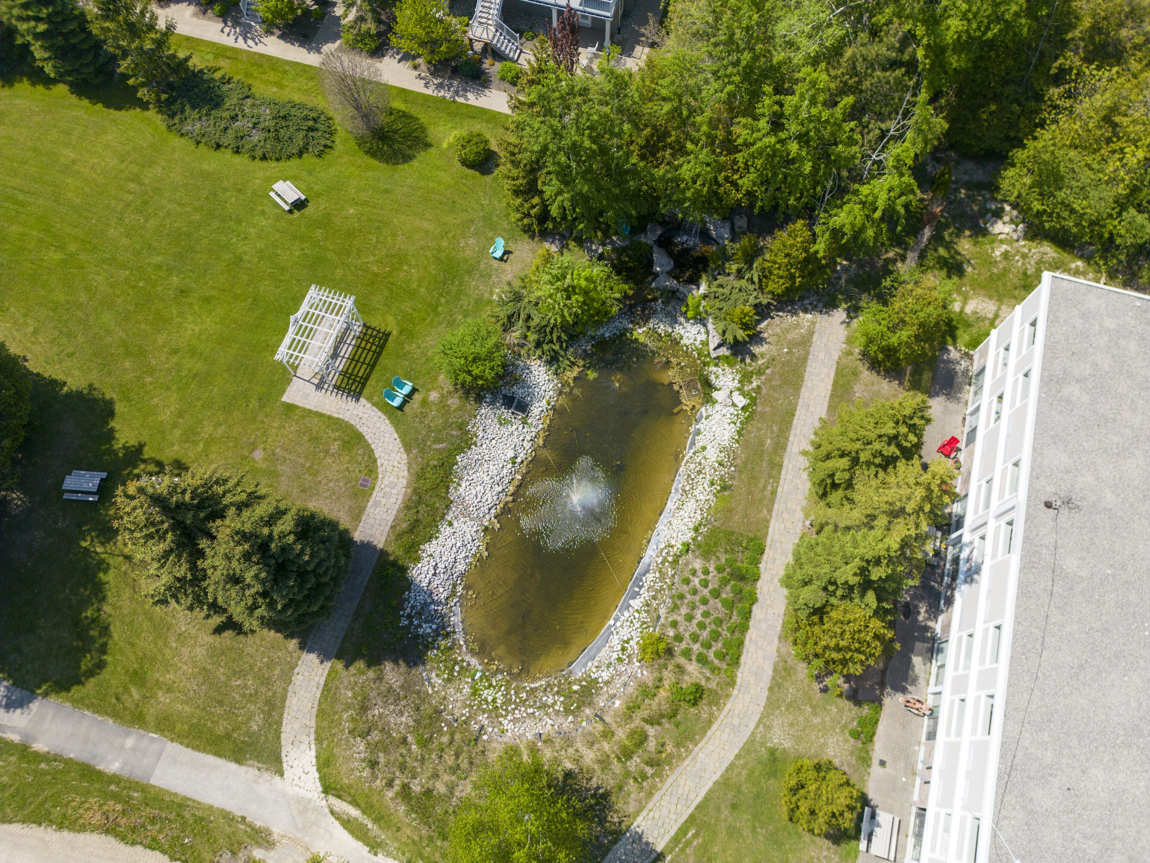 An aerial view of a park with a pond, pathways, benches, and a building.