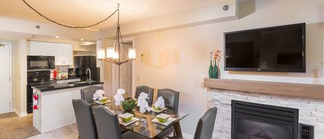 A modern kitchen with a dining area, a flat-screen TV, and a fireplace.