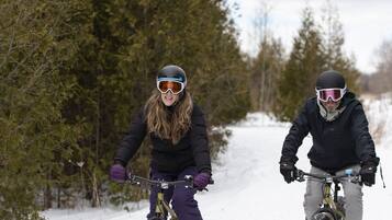 Two people riding bicycles on a snowy path surrounded by trees.